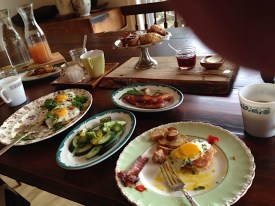 Fresh organic apple cider, pan fried potatoes, eggs, thinly siced cucumber, a plate of bacon and ciarse country sausage below a tray of sweets.